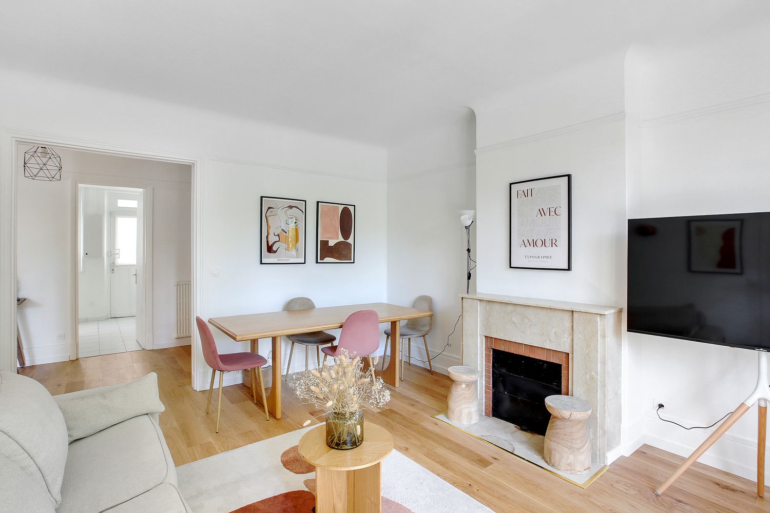 Bright Parisian living room with fireplace, hardwood floors, pink dining chairs, and modern wall art.