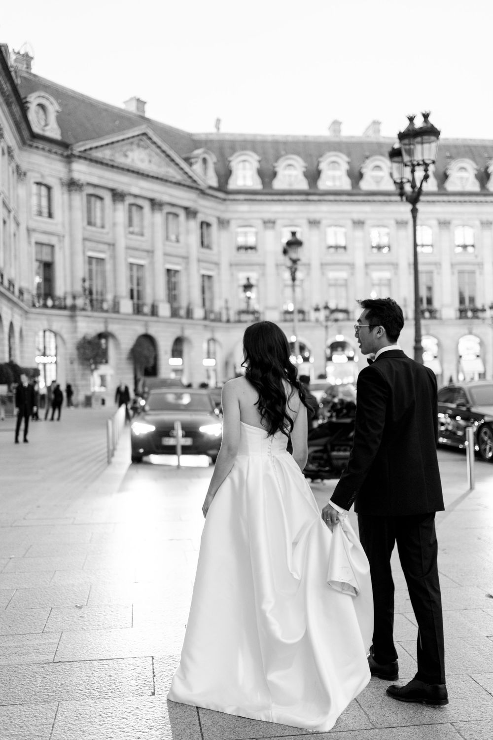 A bride and groom stand together on a European city street with classic architecture in the background.