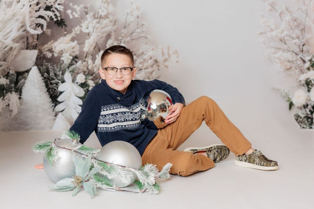 Holiday photo scene with cream couch, silver ornaments, and winter decorations against light background. Clayton NJ Photo Studio