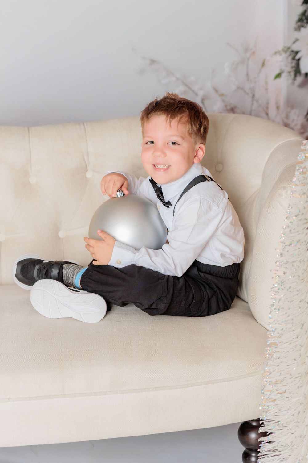 Child relaxing on white couch with silver ornaments in winter-themed photo studio setting. Clayton NJ Photo Studio