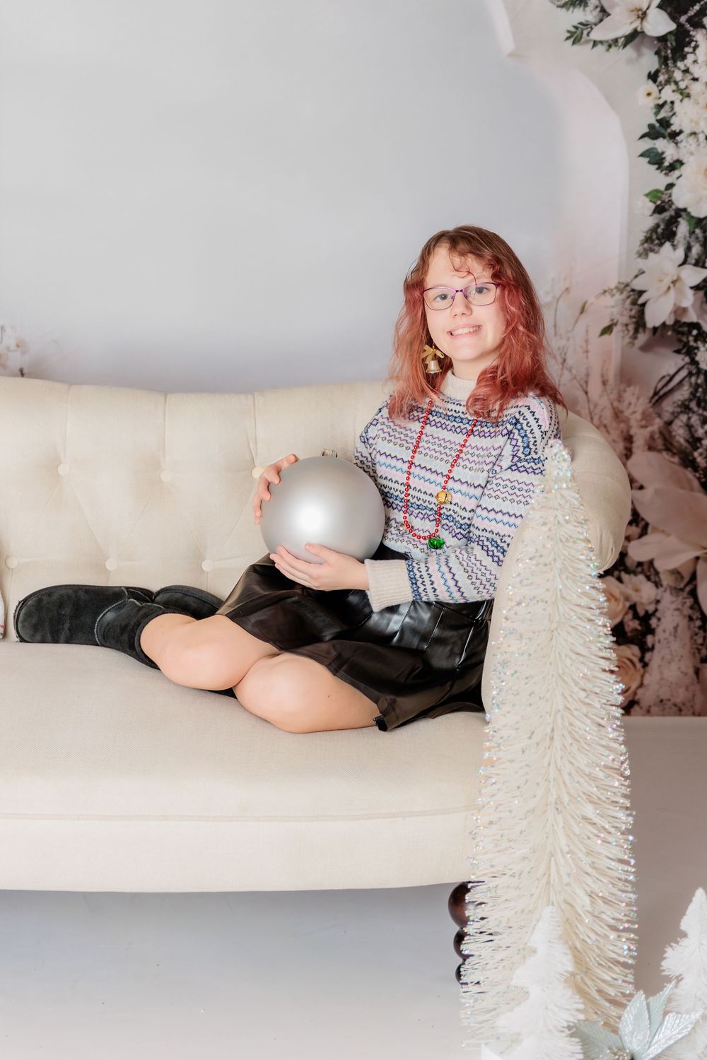 A festive winter photoshoot setup with white Christmas trees and a cream colored couch against a floral backdrop. Clayton NJ Photo Studio