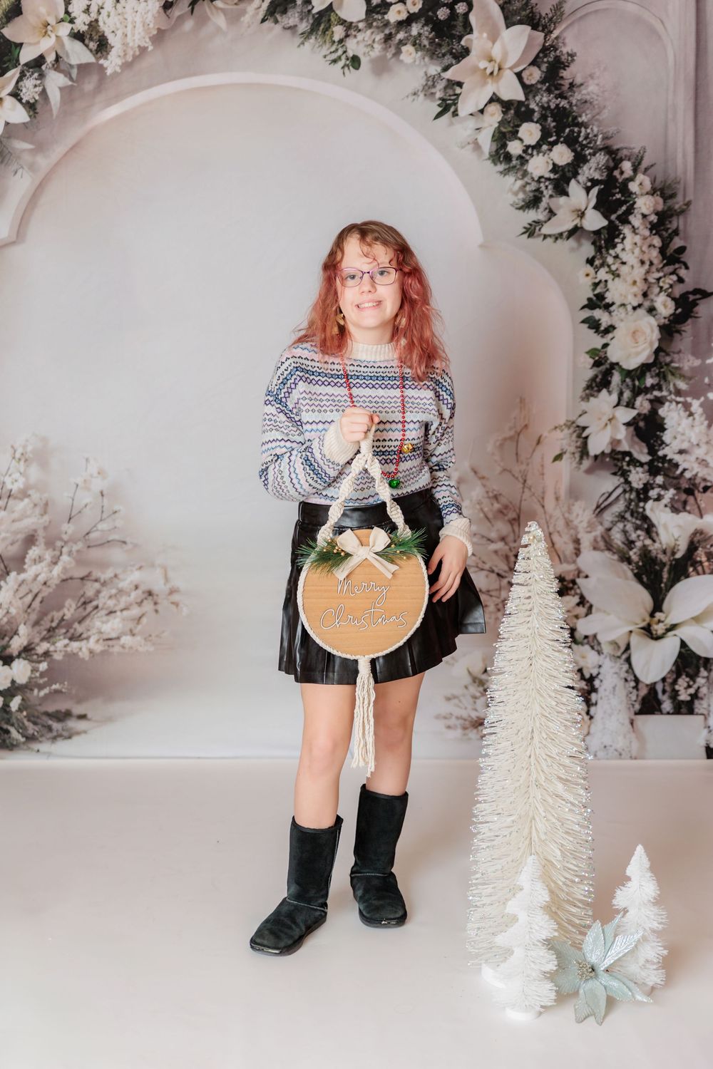 A cozy holiday scene with decorative white trees and winter decor against a floral wall. Clayton NJ Photo Studio