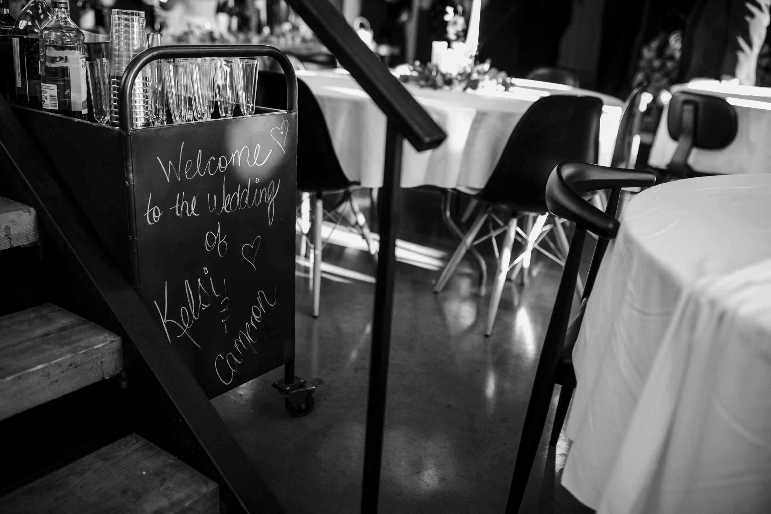A black and white welcome sign stands next to elegant table settings in a dimly lit restaurant or event space.