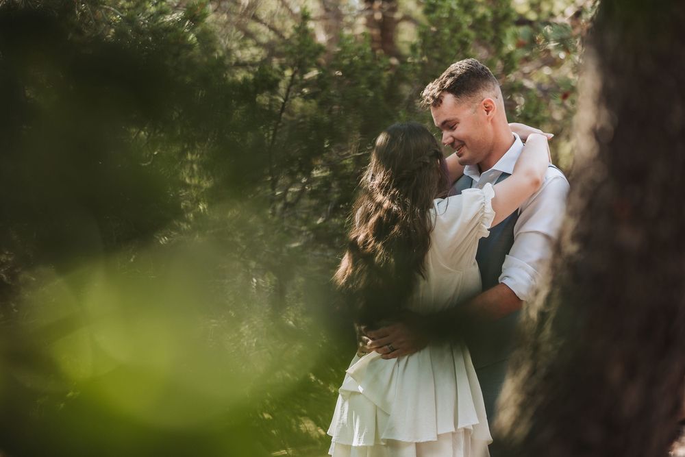 A romantic couple embraces in a sunlit garden setting with green foliage in the background.