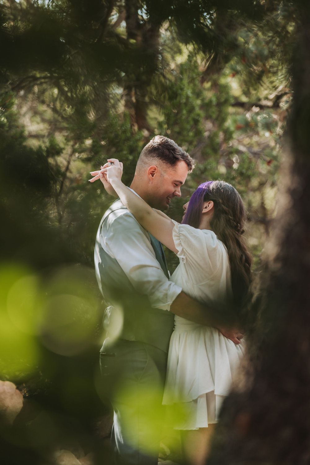 A joyful couple in white dance together outdoors in a romantic forest setting, captured in a sequence of candid moments.
