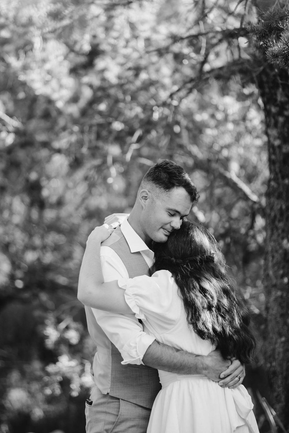 A romantic black and white photo of a couple embracing outdoors with soft bokeh lighting in the background.