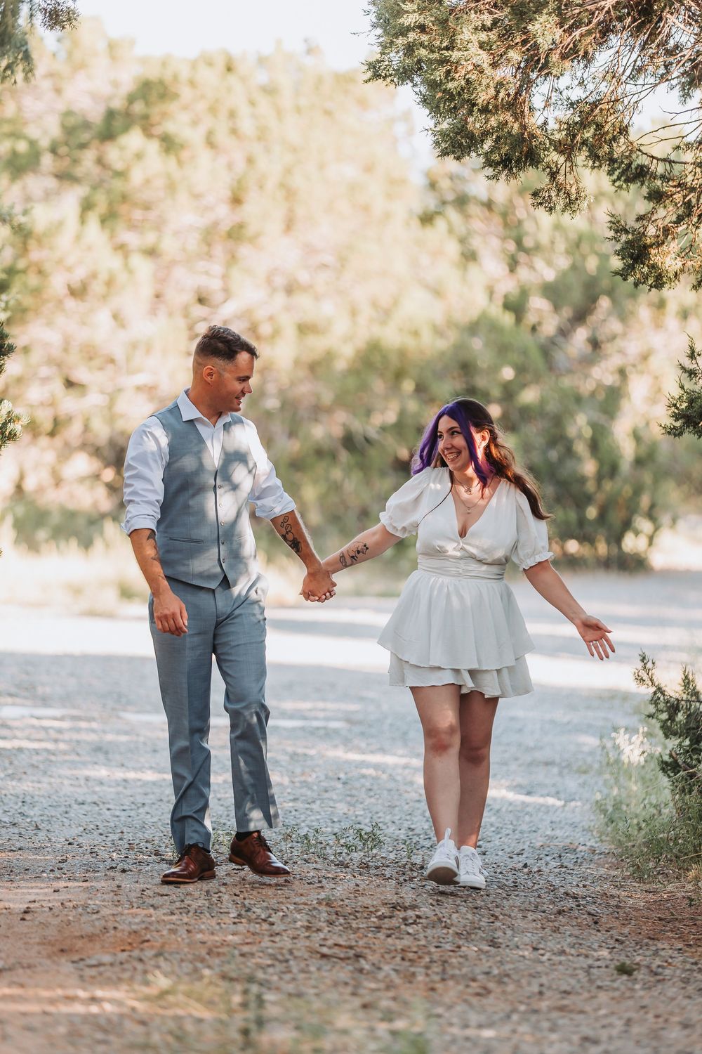 A couple dances playfully on a dirt path surrounded by trees in a romantic outdoor photoshoot sequence.