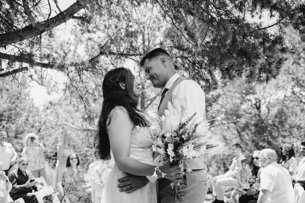Black and white photo of wedding guests mingling under trees at an outdoor reception.