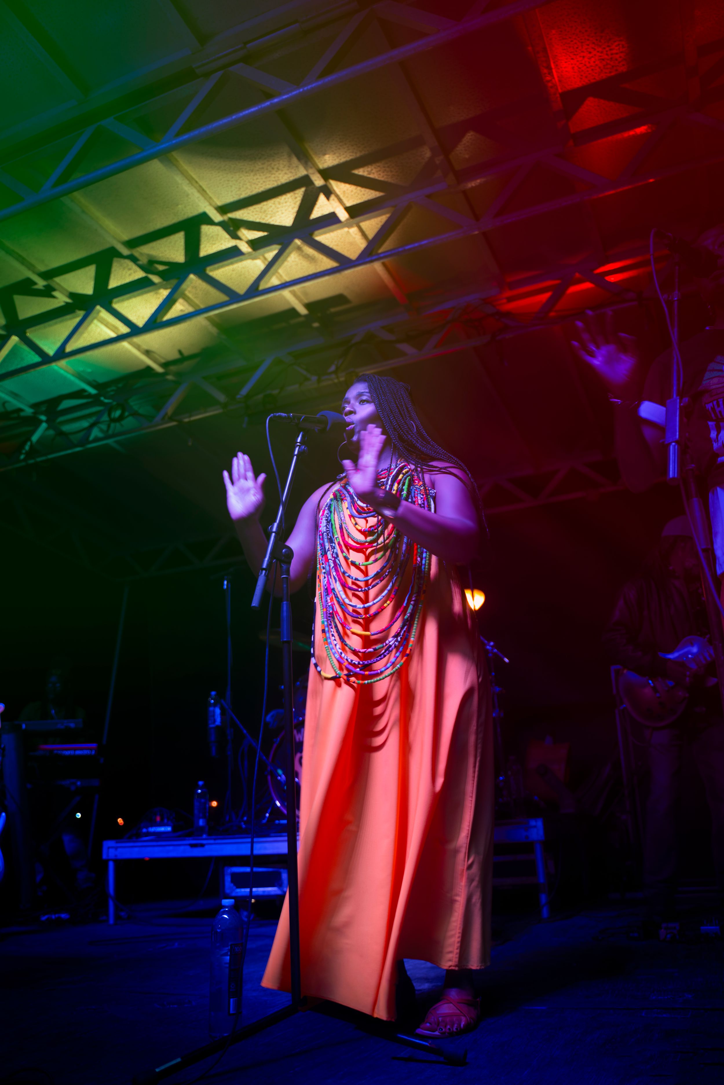 Performer in a red cape on stage illuminated by dramatic colored lighting during a theatrical performance.