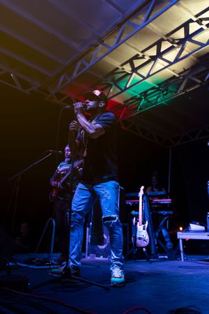 Musicians perform on a dark stage with dramatic blue and red lighting creating silhouettes during a live concert.