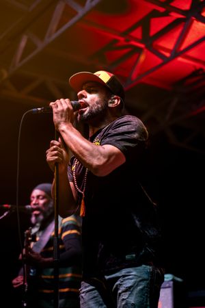 A performer sings passionately into a microphone on a dimly lit stage bathed in dramatic red lighting.