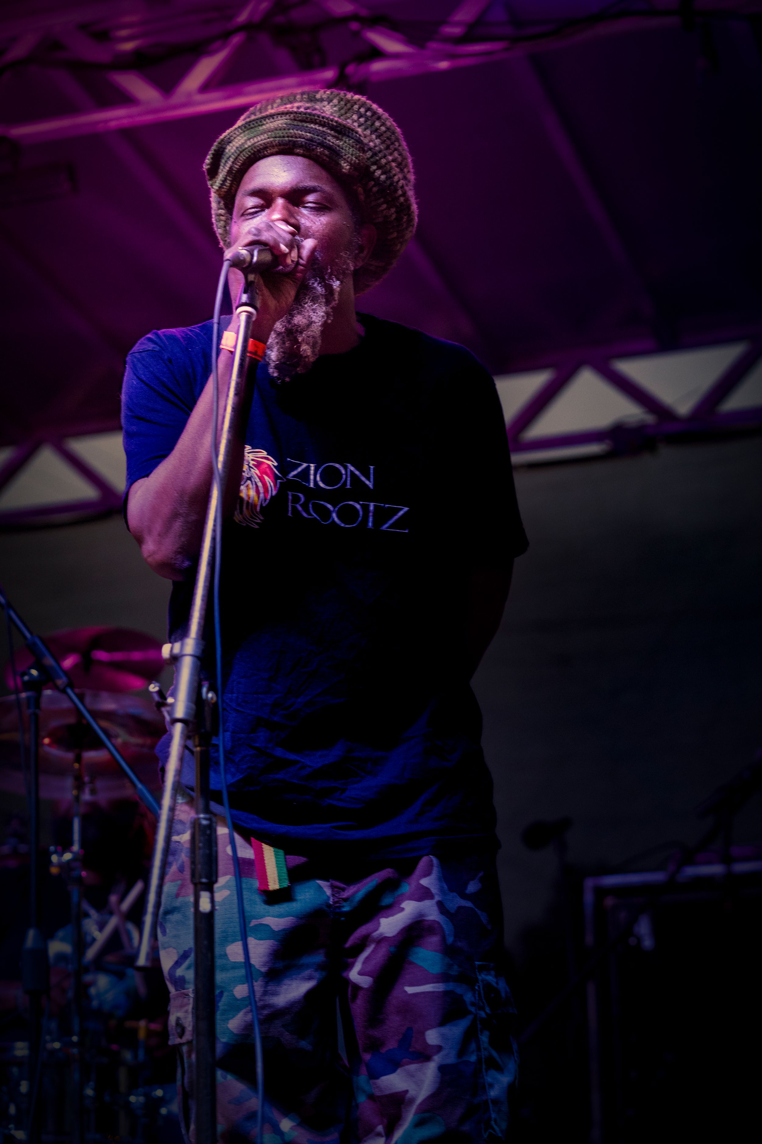 A performer in dark clothing sings into a microphone on stage with purple lighting effects.