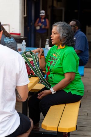 People in bright green shirts sit on yellow chairs at an outdoor event.