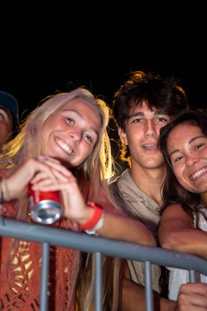 Festival attendees lean against a railing while enjoying an outdoor concert.