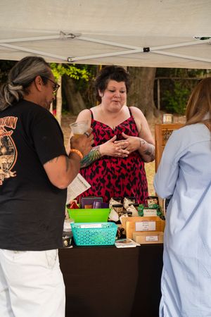 Vendors in white aprons and black shirts work behind tables at an outdoor market or festival booth.