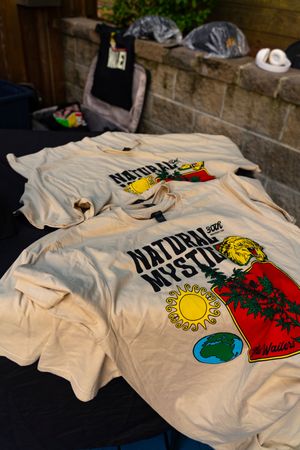 White t-shirts with colorful graphic designs laid out on display at an outdoor market or festival.