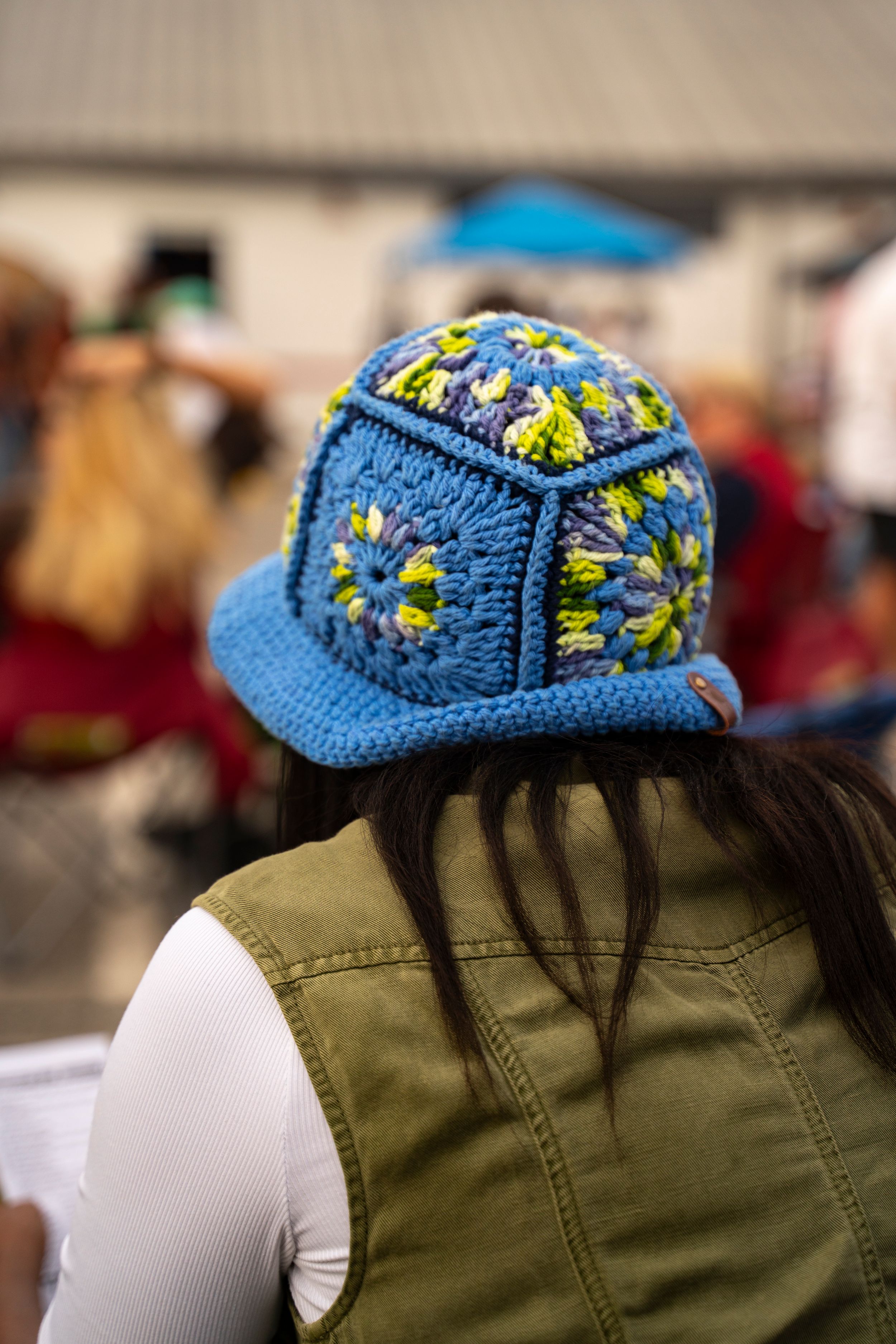 Blue crochet hat with yellow floral pattern displayed on mannequin with olive green shirt.