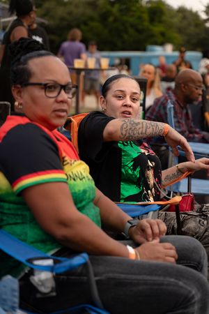 Festival attendees wearing Jamaican-themed clothing sit in chairs at an outdoor event.