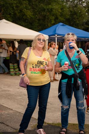 Festival attendees in casual clothing hold drinks while walking through an outdoor event space.