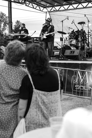 Black and white photo of concert attendees watching performers on an outdoor stage.