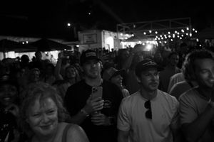 A crowd of people gathered at a nighttime event with string lights visible overhead.