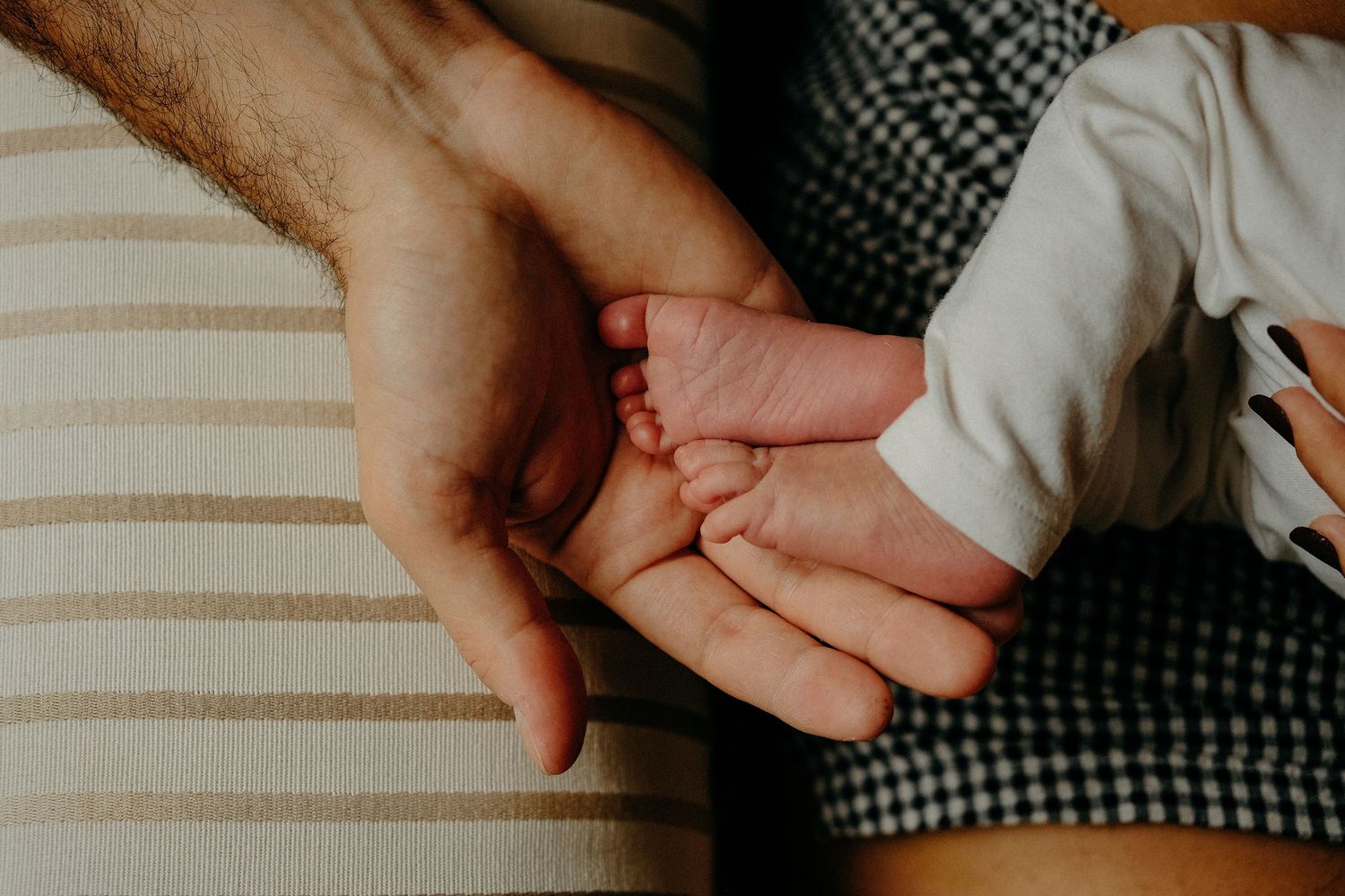 Close-up detail of a parent holding a newborn baby’s tiny hand during a natural lifestyle newborn photography session.