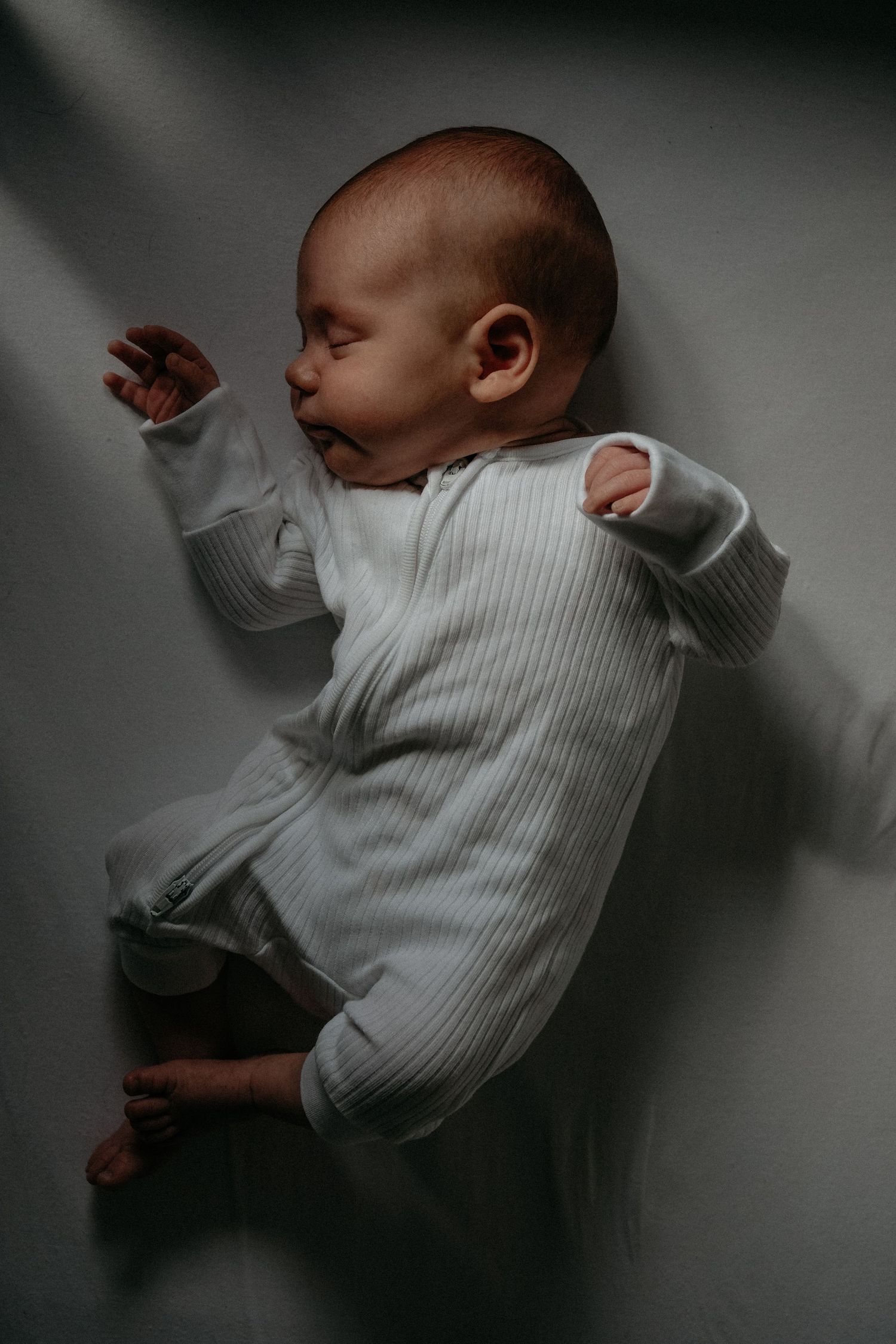 Newborn baby lying peacefully on a bed during a natural lifestyle newborn photography portrait.