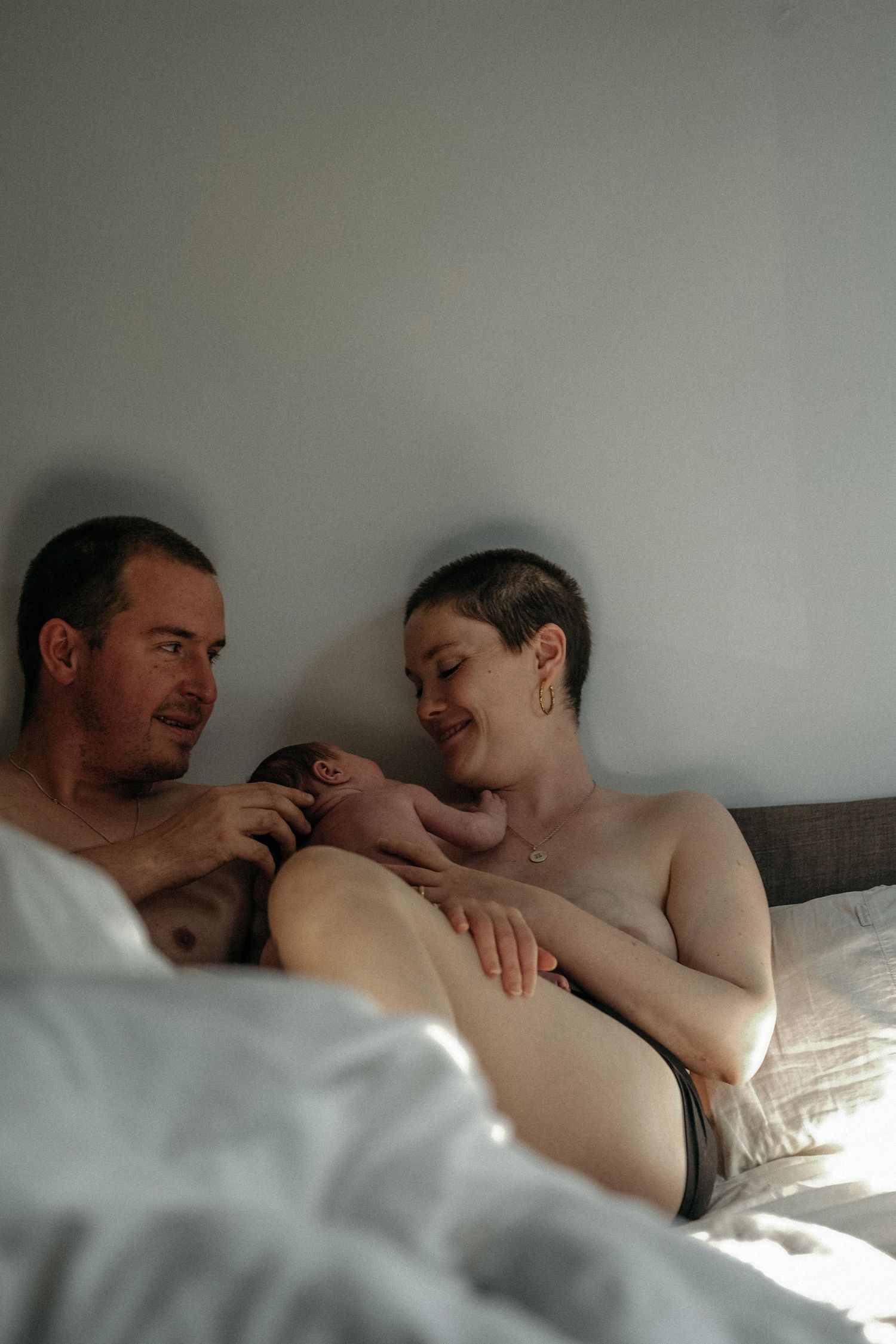 Parents lying together and cuddling their newborn baby during a relaxed in-home lifestyle newborn photography session in Heaton