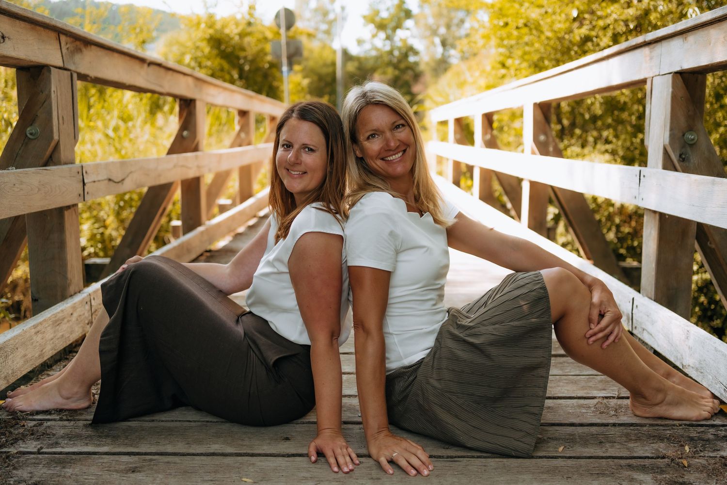 Two people in casual attire laying on wooden steps outdoors during a sunny autumn day.