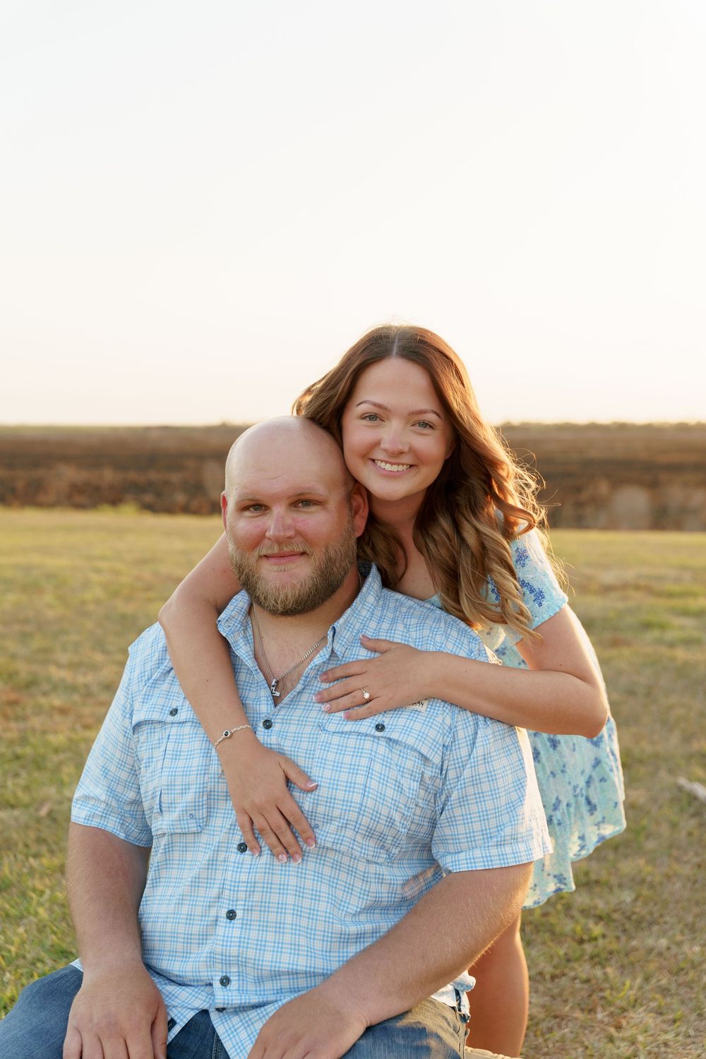 A couple embraces in a sun-lit field during a romantic outdoor photo session at golden hour.