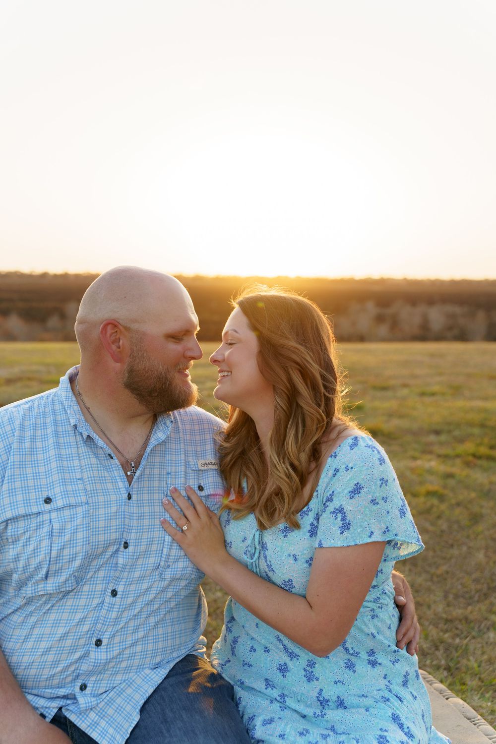 A romantic couple embraces in a sunlit field wearing coordinating blue and white outfits.