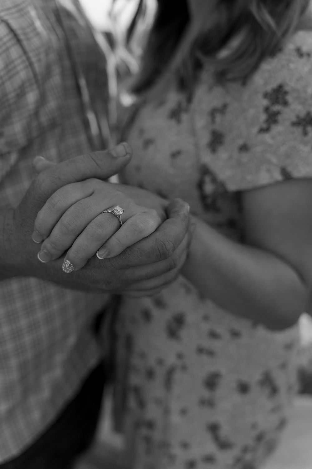 A black and white close-up photo of hands clasped together, with an engagement ring visible on one finger.
