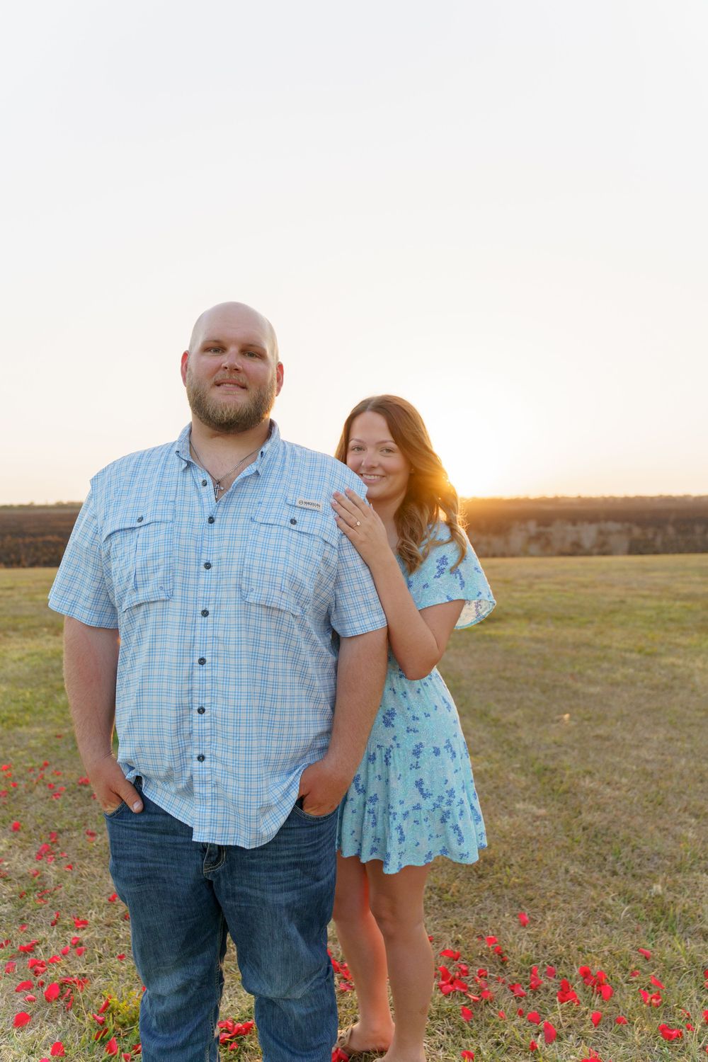 A couple poses playfully in a field of red wildflowers during golden hour.