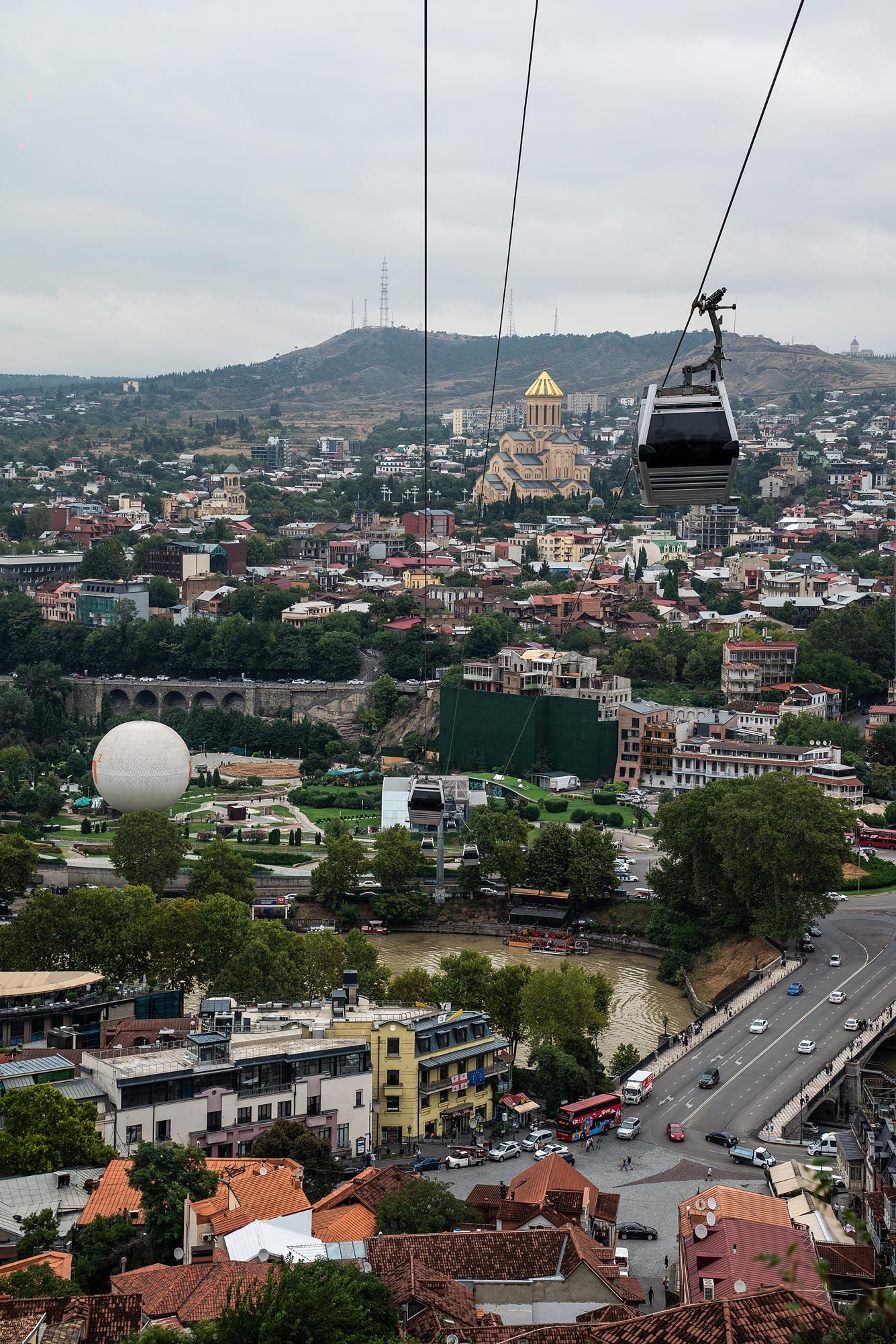 Panoramic cityscape view of Tbilisi, Georgia showing urban buildings, churches and mountains in the background.