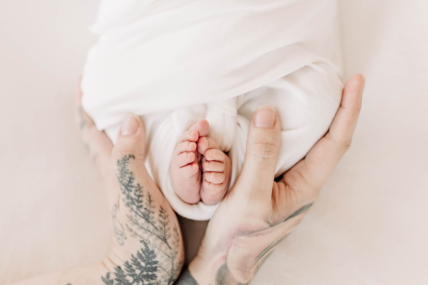 Photograph of newborn baby feet with tiny toes wrapped in soft white blanket against neutral background in mothers hands in Lancaster County
