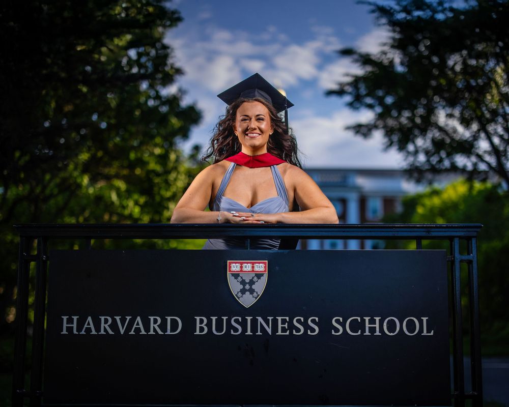 Harvard Business School campus sign and buildings under blue sky with green trees.
