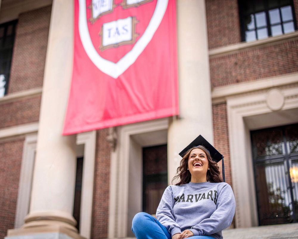 Graduates in caps and gowns celebrate on campus with pink banners hanging in the background.
