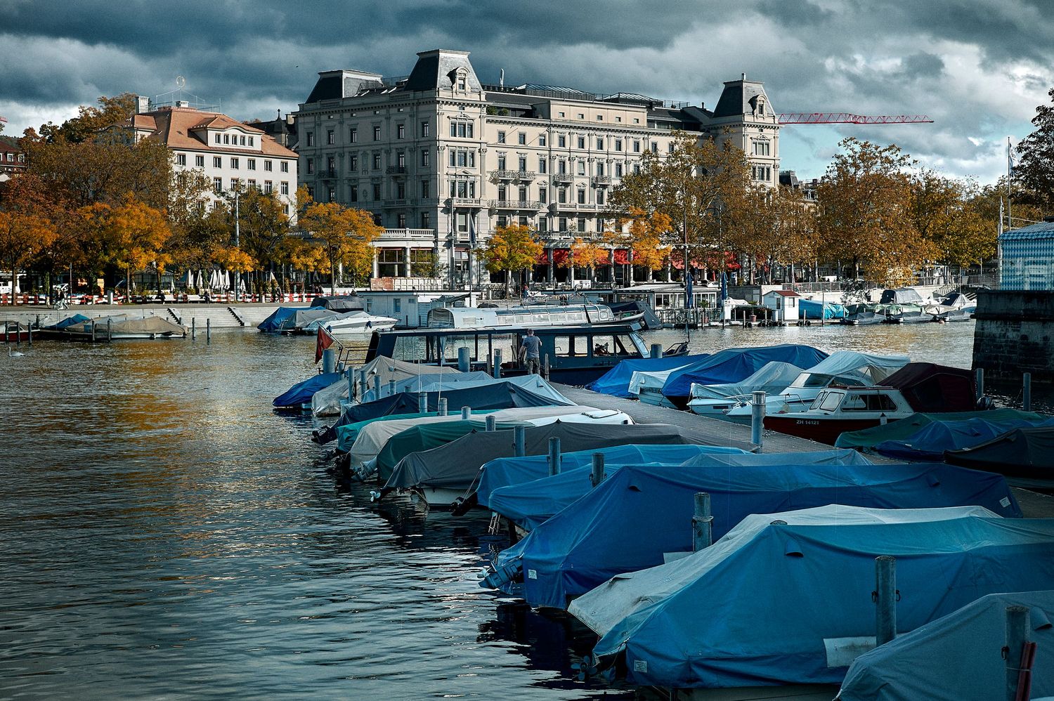 A row of houseboats with blue tarps line the waterfront of Amsterdam's historic canal on a cloudy autumn day.