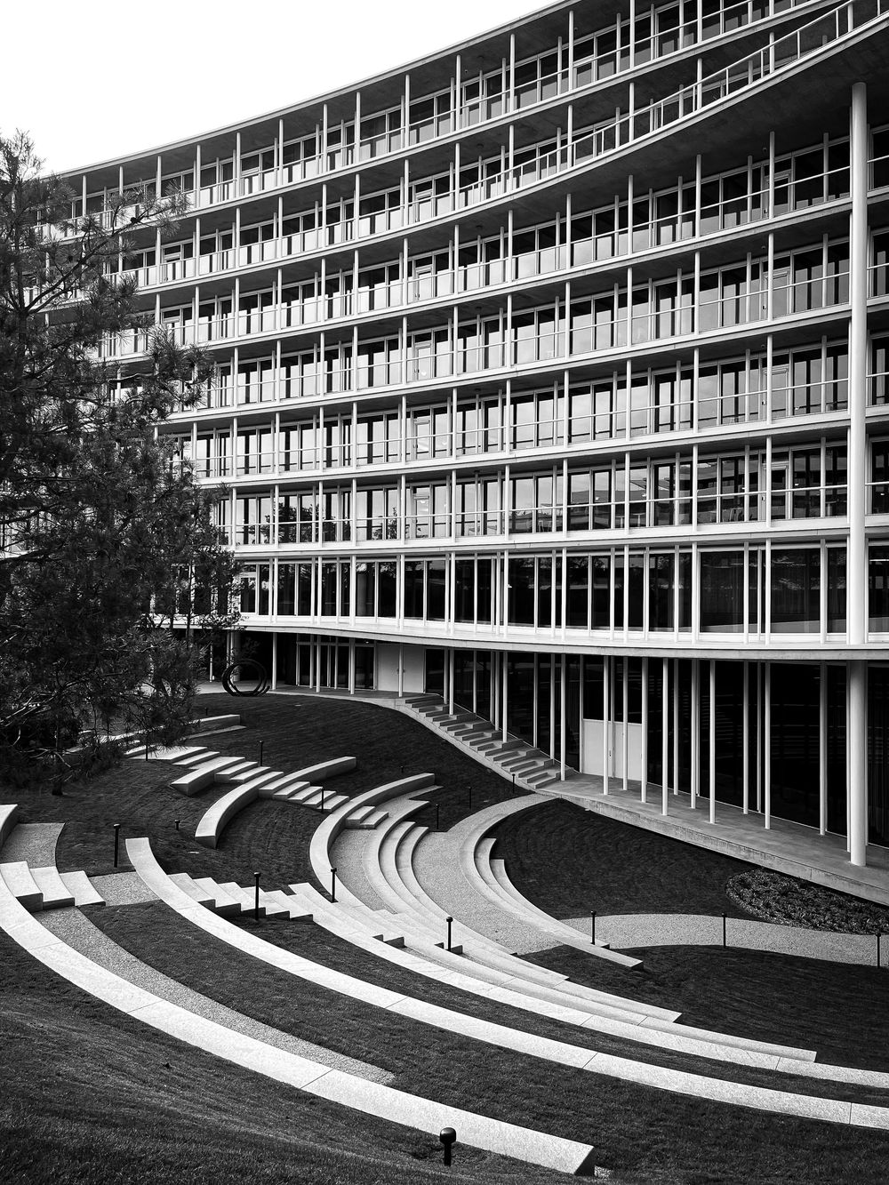 Black and white architectural photo of a modernist building with curved amphitheater steps and geometric balconies.