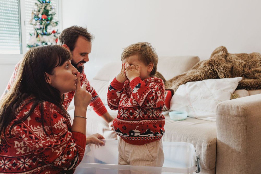 Family wearing matching red holiday sweaters share a joyful moment together in their living room near a Christmas tree.
