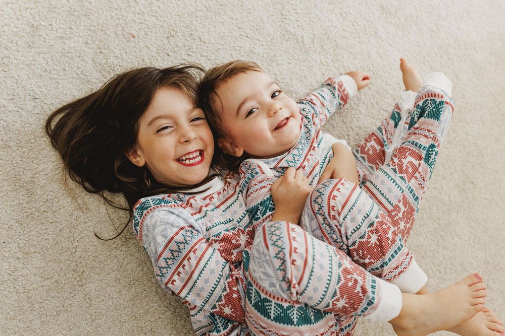 Two children wearing matching floral pajamas lay on the floor laughing and playing together.