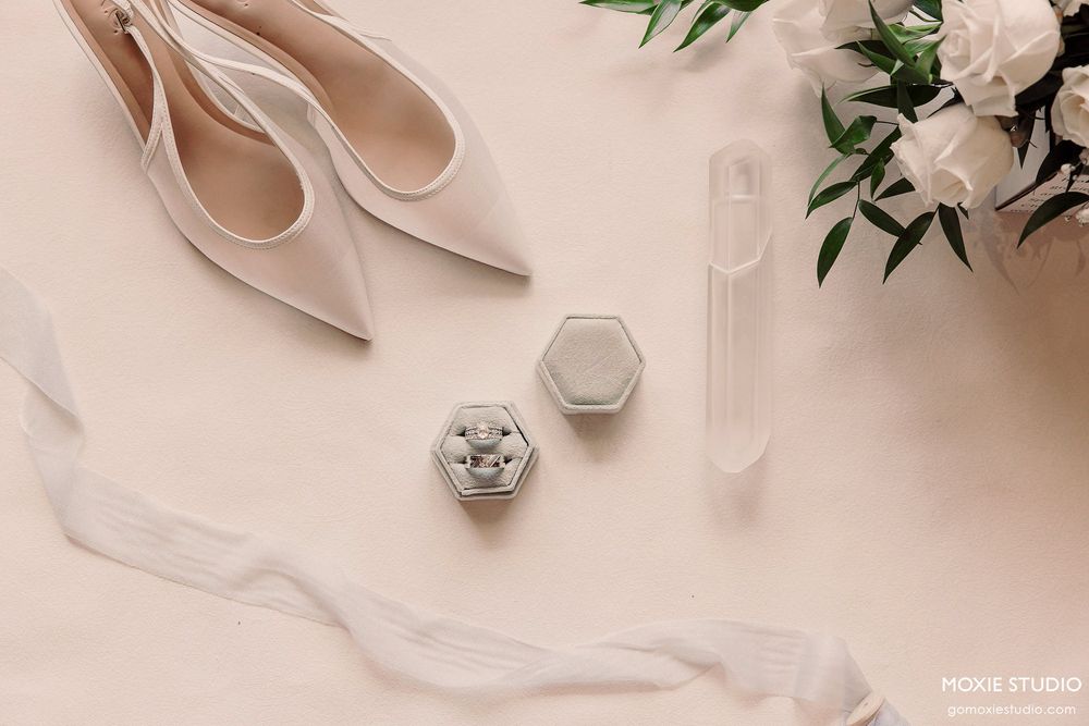 Elegant nude wedding heels and delicate white floral arrangements on a soft beige background create a romantic bridal setting.