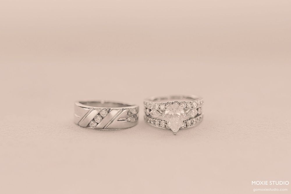 Two elegant silver wedding rings with diamond accents displayed on a soft beige background.