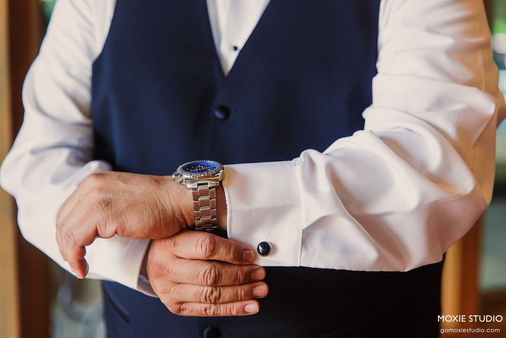 Close-up view of someone adjusting their watch while wearing a navy vest and white dress shirt.