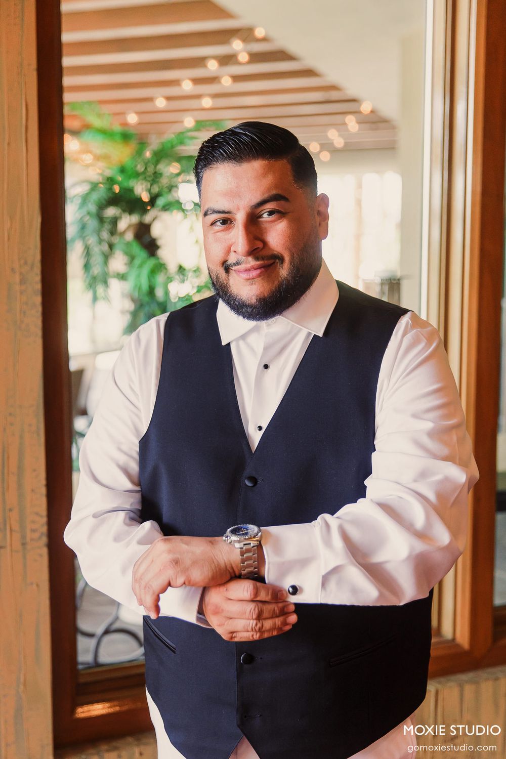 Professional portrait in formal attire standing in elegant venue with wooden beams and warm lighting.