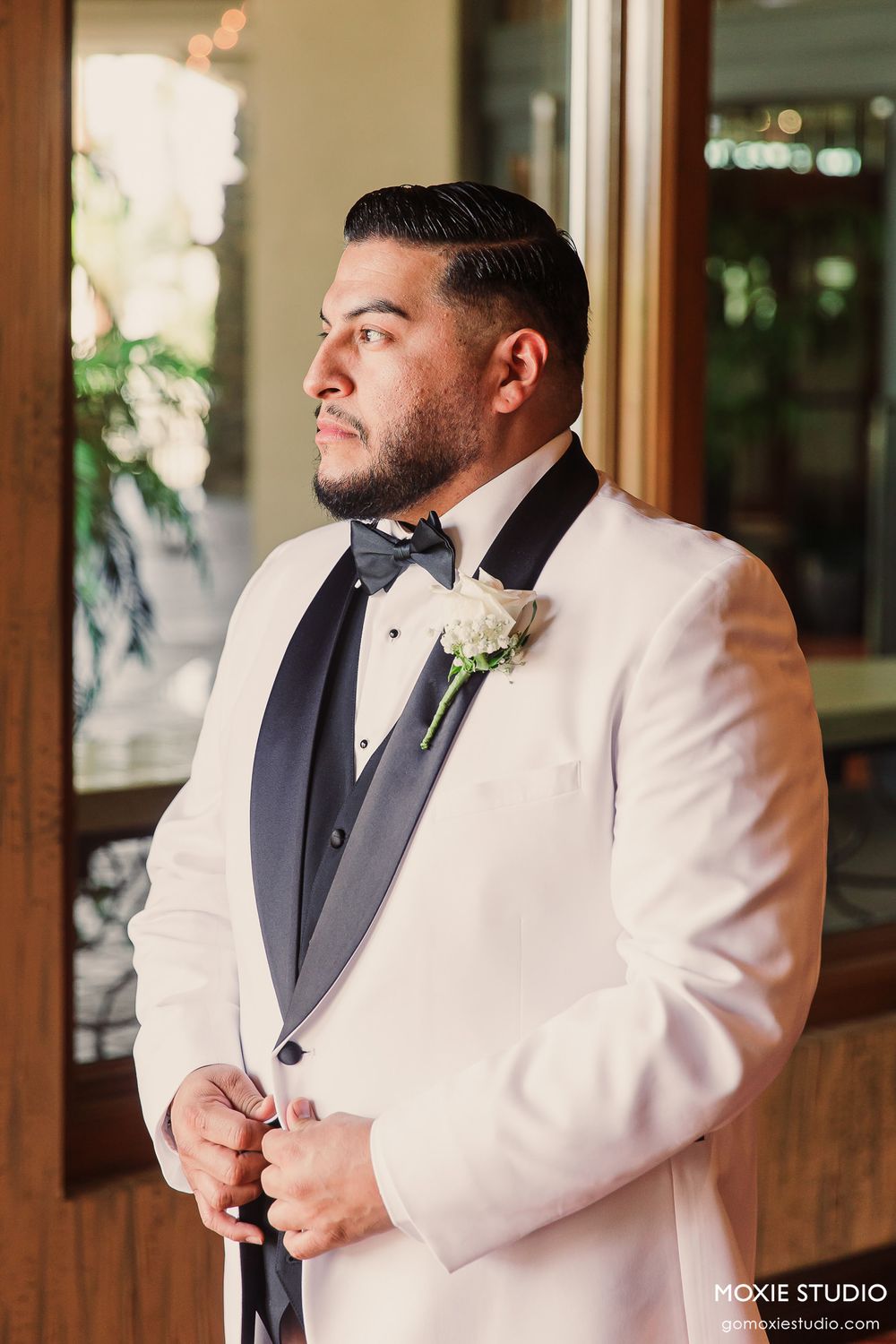 Groom in white tuxedo jacket and black bow tie adjusts his cuff links before wedding ceremony.