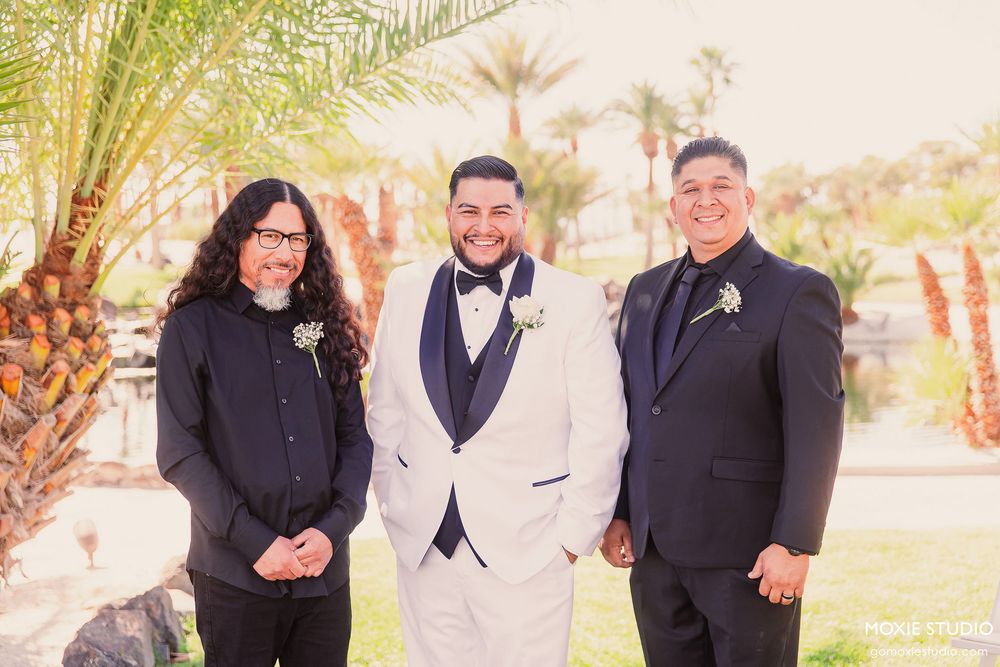 Wedding party poses together outdoors under palm trees during a formal celebration.