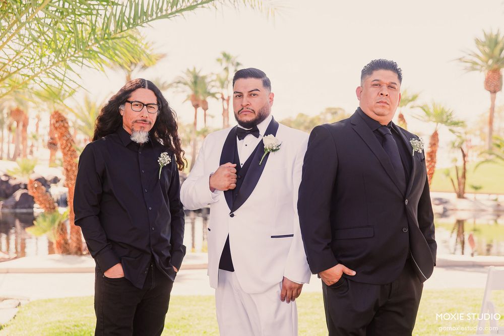 Wedding party members in formal black attire gathered outside on a sunny day.