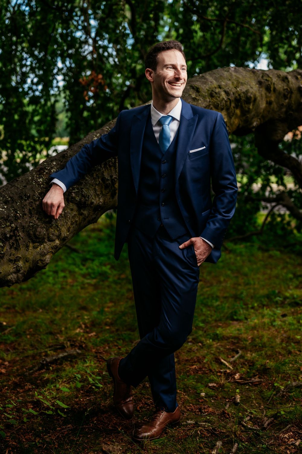 Person in navy suit poses playfully outdoors in a series of candid shots against a natural forest backdrop.