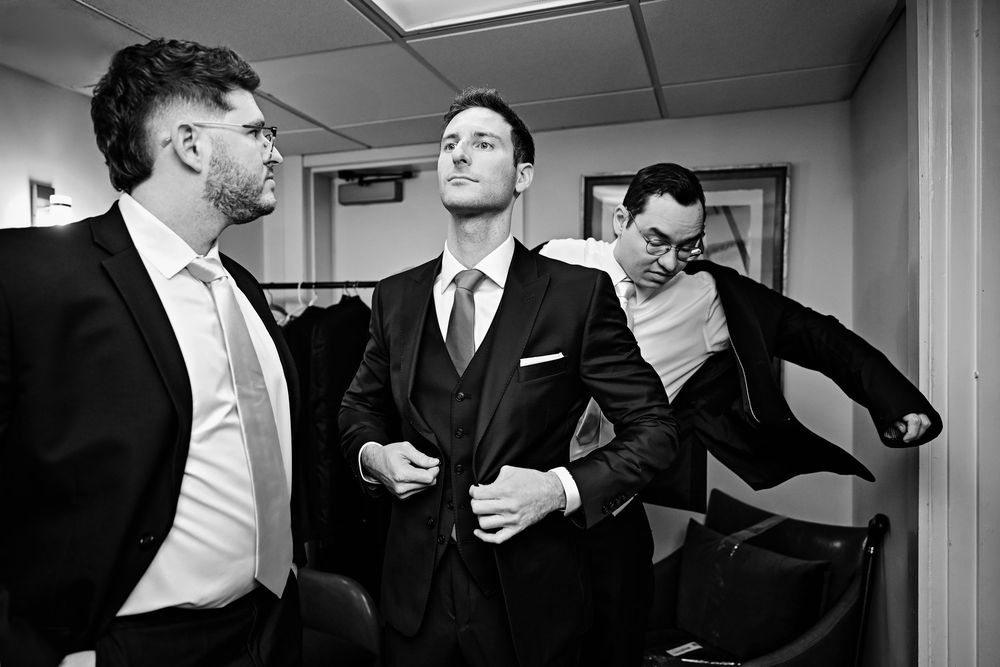 Black and white photo of groomsmen sharing laughs in a formal setting.